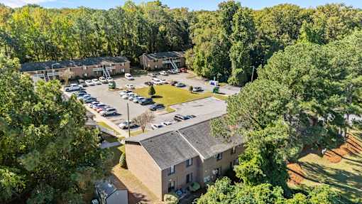Drone view of the parking lot surrounded by trees and a brick complex building in the background.