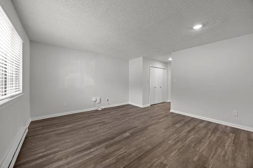 A white painted room with wooden flooring and the side of a window.