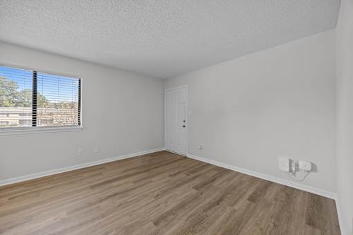 An open room with wooden flooring and a window with blinds.