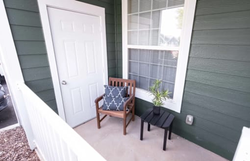 A white door is on the left of a porch with a chair and a small table.