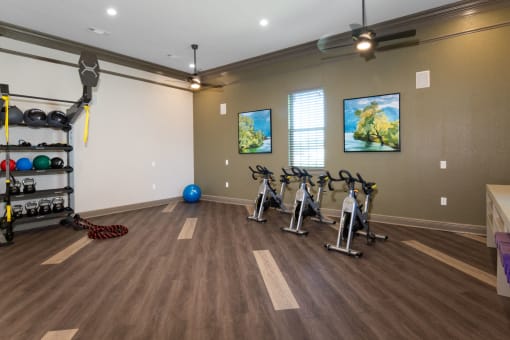 a fitness room with exercise bikes and weights on a wooden floor