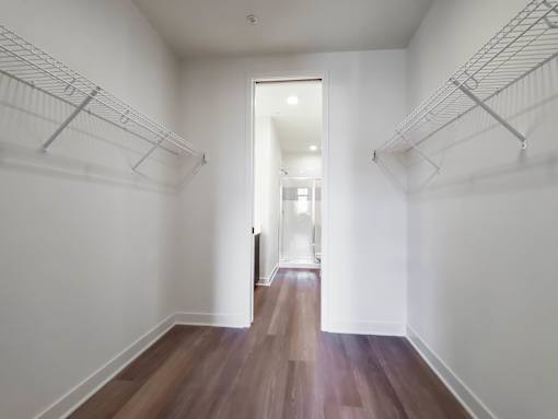 A hallway with white walls and wood flooring leading to a door.
