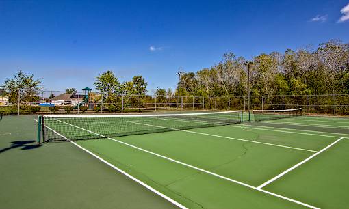 A tennis court with a net and trees in the background at Evergreen Luxury Apartments, Merrillville, IN, 46410