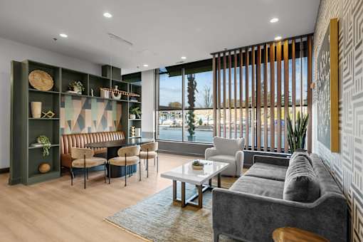 A modern living room with a grey sofa, wooden chairs, and a glass table.