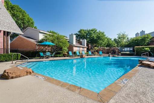 An apartment swimming pool surrounded by a stone border and a few chairs at 1601 Eastchase Pkwy in Fort Worth, TX.