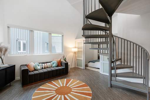 A living room with a spiral staircase and a black couch.