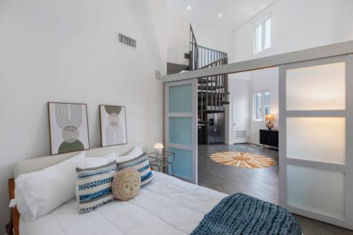 A bedroom with a bed, pillows, and a staircase in the background at Fusion Hollywood Apartments.