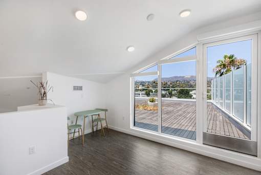 A loft with a table and chairs and a view of the outside through a glass door at Fusion Hollywood Apartments.