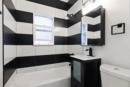 A black and white bathroom with a tub, sink, and mirror at Brookmore Pasadena, CA.