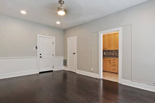 A studio apartment in Pasadena, CA with white walls and a wooden floor with a door and a window at Brookmore Apartments.