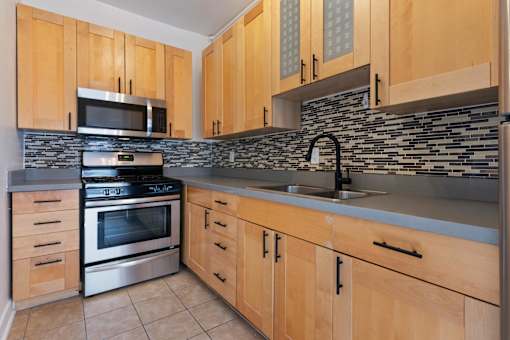 A kitchen with wooden cabinets and a stone backsplash at Brookmore Apartments Pasadena, CA