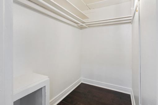 A white closet with a wooden floor and a white shelf.