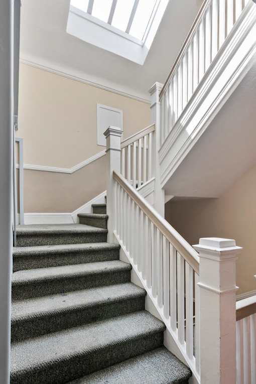 A staircase with a grey carpeted runner and white balusters at Brookmore Apartments