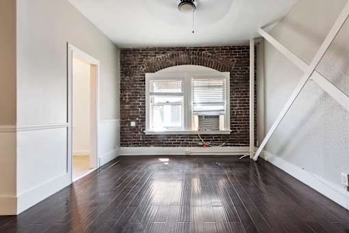 A studio apartment with a brick wall and wooden floors at Brookmore Pasadena apartments.