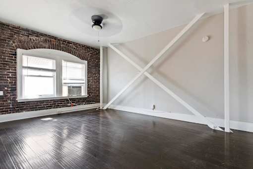 An apartment living room with a brick wall and wooden flooring at Brookmore Apartments in Pasadena, CA.