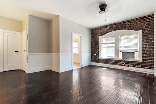 A living room with a brick wall and wooden floors leading into a kitchen at Brookmore Apartments.