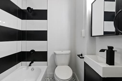 A white toilet sits next to a sink in a black and white bathroom at Brookmore Apartments in Pasadena, CA