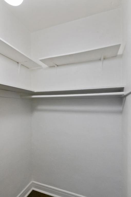 A white wall with a light on top and a shelf below it in a studio apartment closet.
