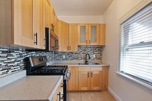 A studio apartment with a kitchen with wooden cabinets and a black stove top oven at Brookmore Apartments.