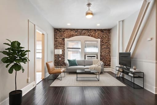 A living room with a brick wall and a grey couch.