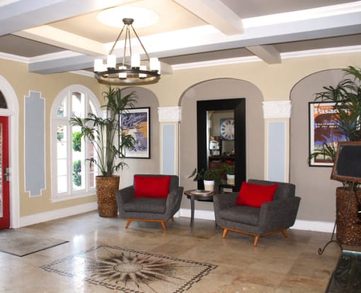 Pasadena Brookmore apartments lobby seating area with large gray midcentury chairs with red pillows on a marble tile floor.