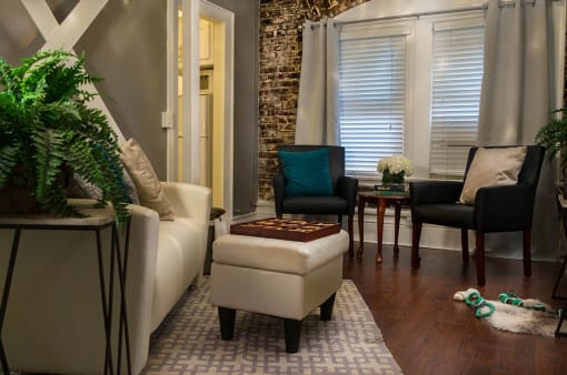 Pasadena Brookmore Suite with cream sofa, small sitting area by window, an open door to kitchen, and Exposed Brick Wall