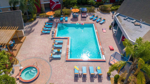 Aerial view of L-shaped community pool at Fusion Apartments in Orlando, FL. Pool is next to pool house, wood trellis, and round hot tub.