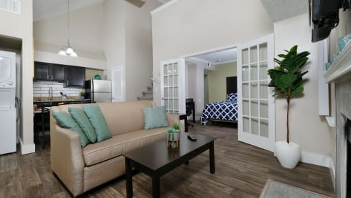 Fusion apartments complex Orlando, FL furnished apartment living room with tan couch with teal pillows, espresso coffee table, and glass French doors open to bedroom.