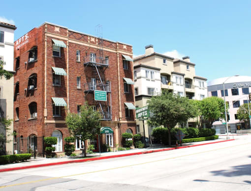 Street view of Brookmore apts in Pasadena CA. Four story brick building with striped awnings, fire escape, and "now leasing" sign.