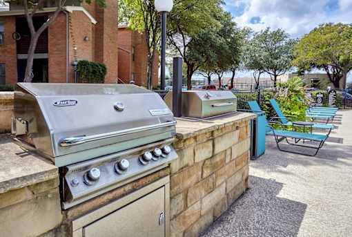 A BBQ grill is on a patio with a blue chair and a brick wall at 1601 Eastchase Pkwy in Fort Worth, TX.