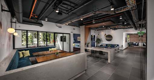 Fusion Encore Hollywood Apartments clubhouse with a long table and chairs, a sofa with cushions, and a large window with a view of trees.