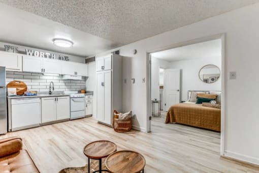 Fusion Fort Worth Apartments renovated kitchen area in Haltom City, TX with light wood plank flooring and subway tile backsplash, white appliances, and large bedroom door.