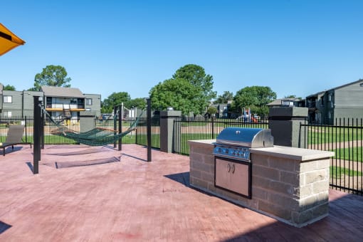 barbecue area and hammock lounge at Fusion Fort Worth in Haltom City, TX next to large green field with black iron fence.