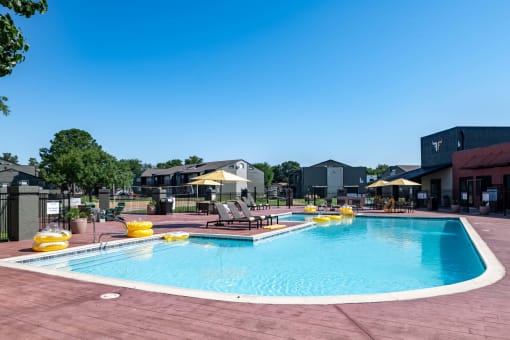 Community swimming pool at Fusion Fort Worth apartments in Haltom City, TX with yellow inflatables and lounge chairs with umbrellas
