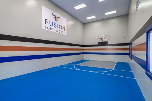 Apartments with indoor basketball and racquetball court at Fusion Fort Wort with blue floor and apartment logo on the wall