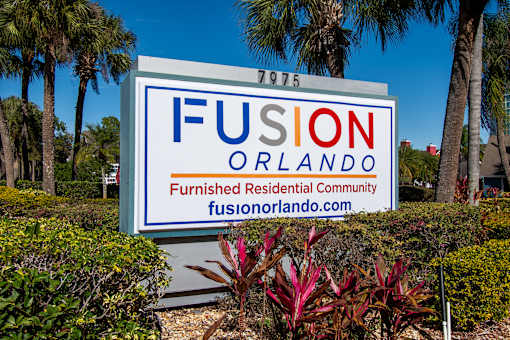 A sign for Fusion Orlando, a furnished residential community, is displayed in front of some trees.