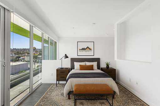 A bedroom with a bed, nightstand, and a window with a view of the street.
