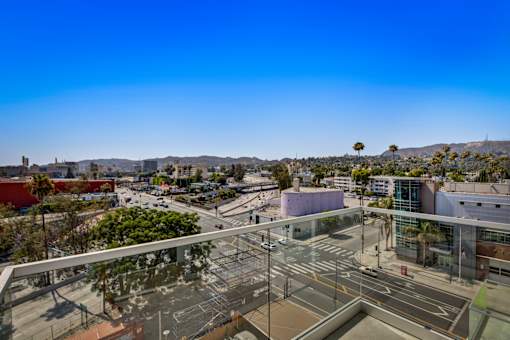 A view of Los Angeles from a private balcony at Fusion Hollywood overlooking a city street with buildings and palm trees.