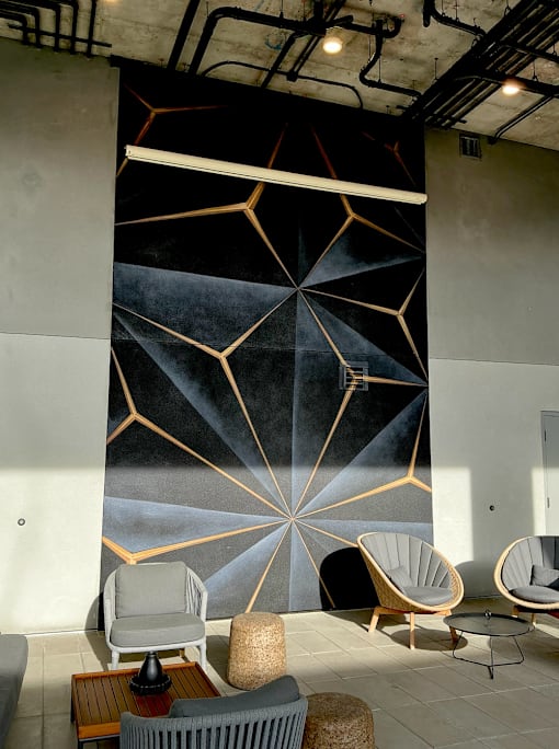 Fusion Hollywood Apartments (previously Alta Ink Apartments) seating area with a large geometric mural on the wall and several chairs and tables.