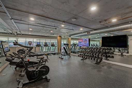 Fusion Hollywood fitness center with a row of stationary bikes and a TV screen.