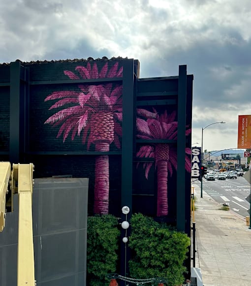A large mural of pink palm trees on a dark wall at Fusion Hollywood Apartments in Los Angeles (previously Alta Ink Apartments).
