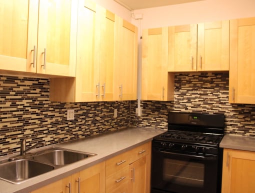 Kitchen in one bedroom brookmore apartment in Pasadena. Modern wood cabinets with silver pulls, multicolored tile backsplash, and black gas stove