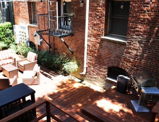 Brookmore Pasadena ca apartments back patio surrounded by greenery and brick wall with wicker patio furniture, stained wood deck, and grilling station.
