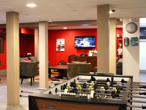 Brookmore apartments rec room with red walls. Features a football table and TV room with couches, console, and coffee table.