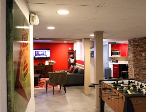 Brookmore apartments rec area with foosball table; kitchen area with toaster, microwave, and red cabinets; and living room with TV and couches.
