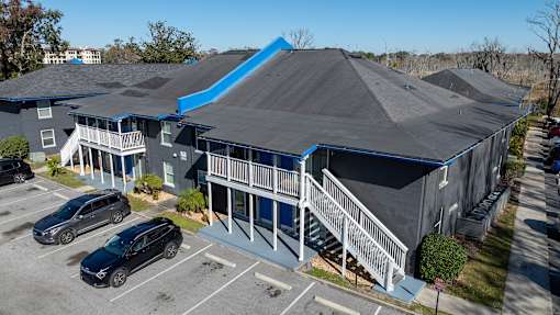 A large grey building with a blue roof and a parking lot in front at Mandarin Bay Apartments on San Jose Blvd