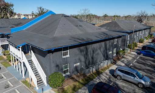 A grya building with a blue roof is surrounded by a parking lot at Mandarin Bay Apartments on San Jose Blvd