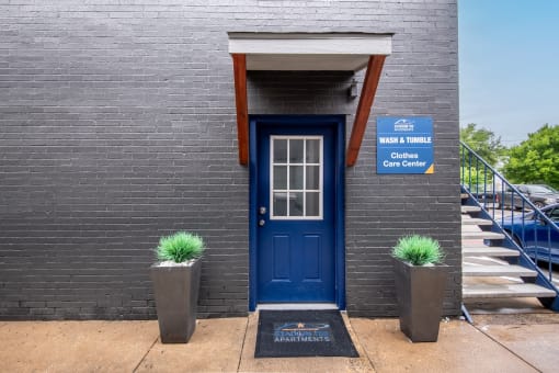 Blue door on the side of Stadium 700 Apartments in Arlington, TX next to a sign that reads "Wash & Tumble: Clothes Care Center"