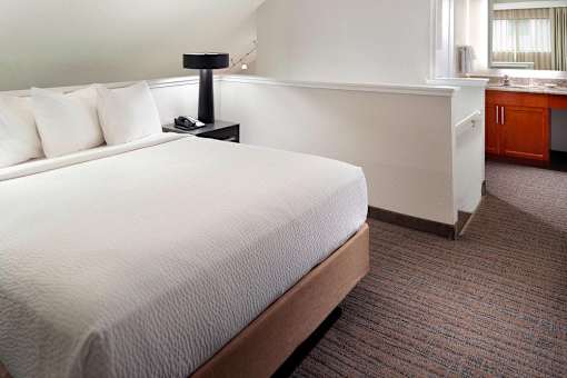 A bed with white pillows and a white bedspread in a room with a carpeted floor in a two bedroom apartment at Fusion Buckhead.
