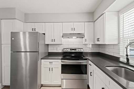 A modern kitchen with a stainless steel refrigerator, stove, and white cabinets at Mandarin Bay Apartments.